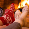 Three sets of winter stocking feet sitting in front of a fire in fireplace