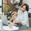 Mother on phone, working at her desk with child on her lap